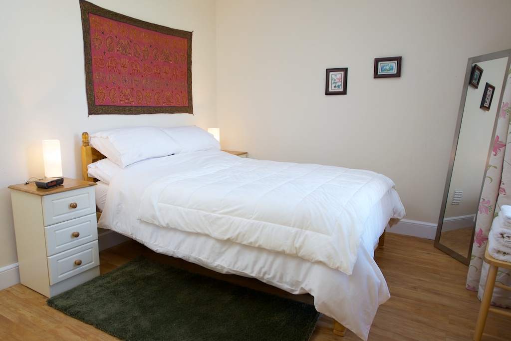 Image of bedroom showing double bed with white bed linen, bedside drawers and mirror in Cosaig Self-Catering Innerleithen